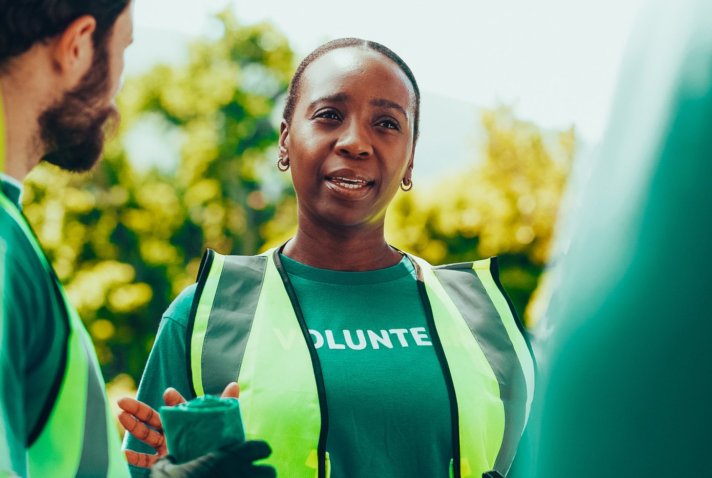 A smiling volunteer in a safety vest at a community clean-up