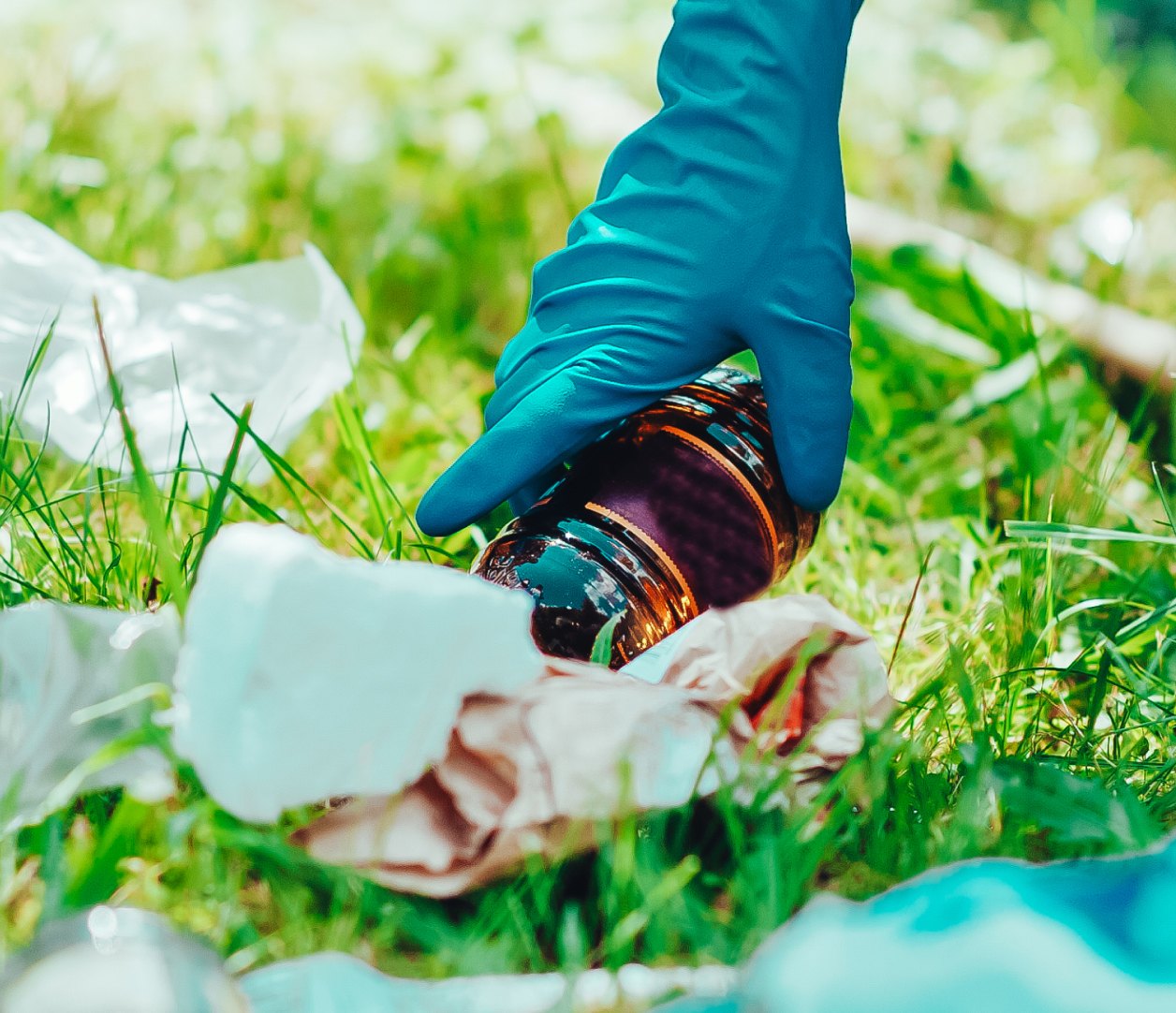 A gloved hand picking up plastic waste from the grass